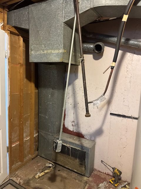 Furnace unit and ductwork in a basement corner, with a long metal pipe and some tools present.