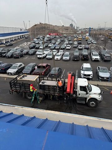 Truck with tanks being worked on in a parking lot. Two workers, cars, and a crane in the background.