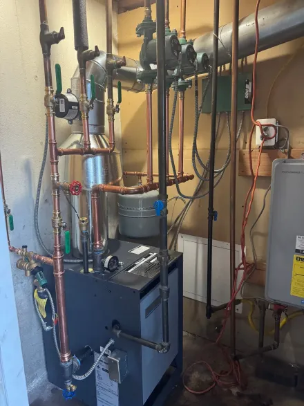 A residential hydronic heating boiler with connected copper piping, valves, and electrical wiring in a basement setting.