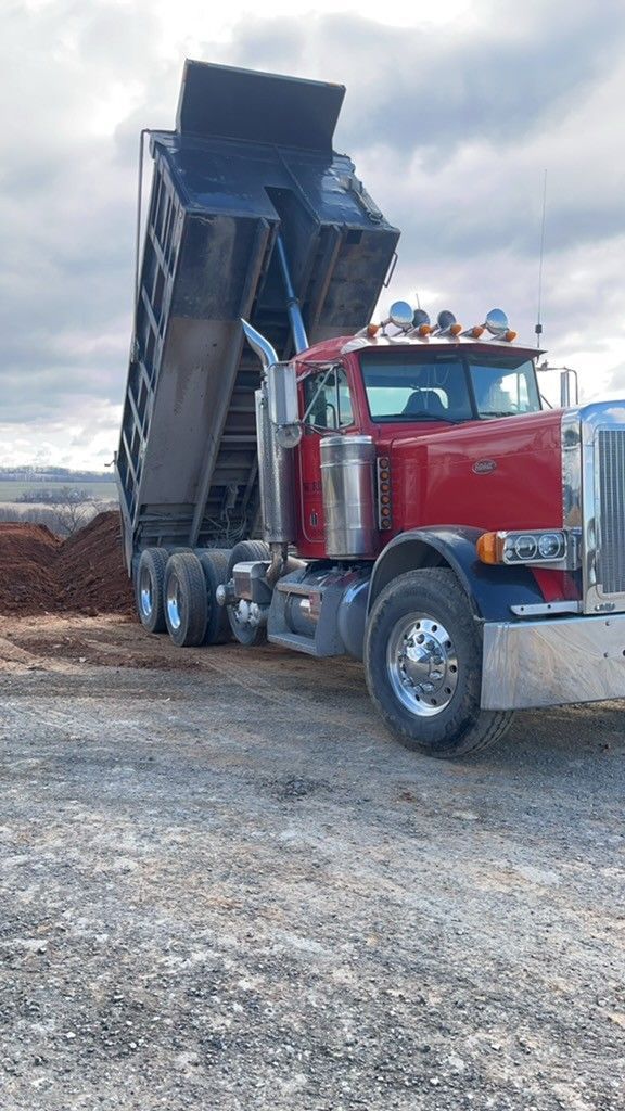 A red dump truck is sitting in a gravel lot.
