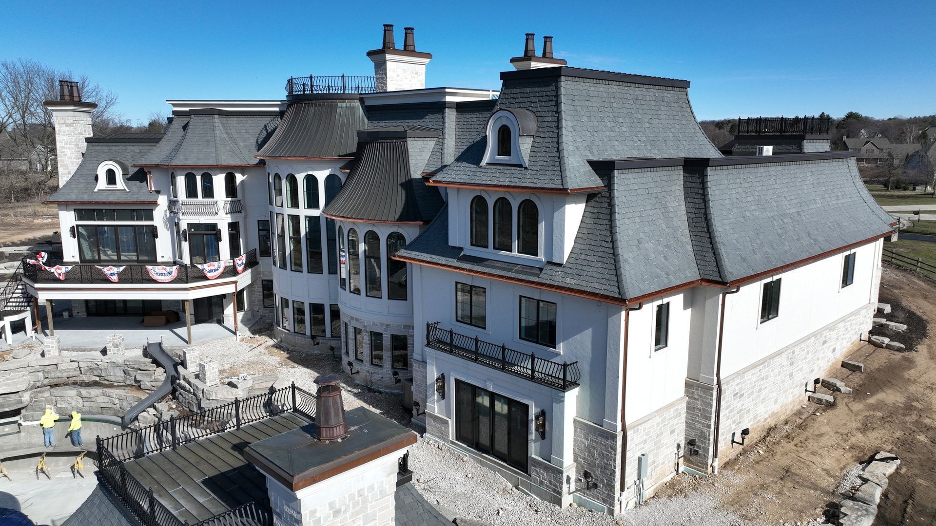 Large white mansion with gray roof and stone accents; construction site.