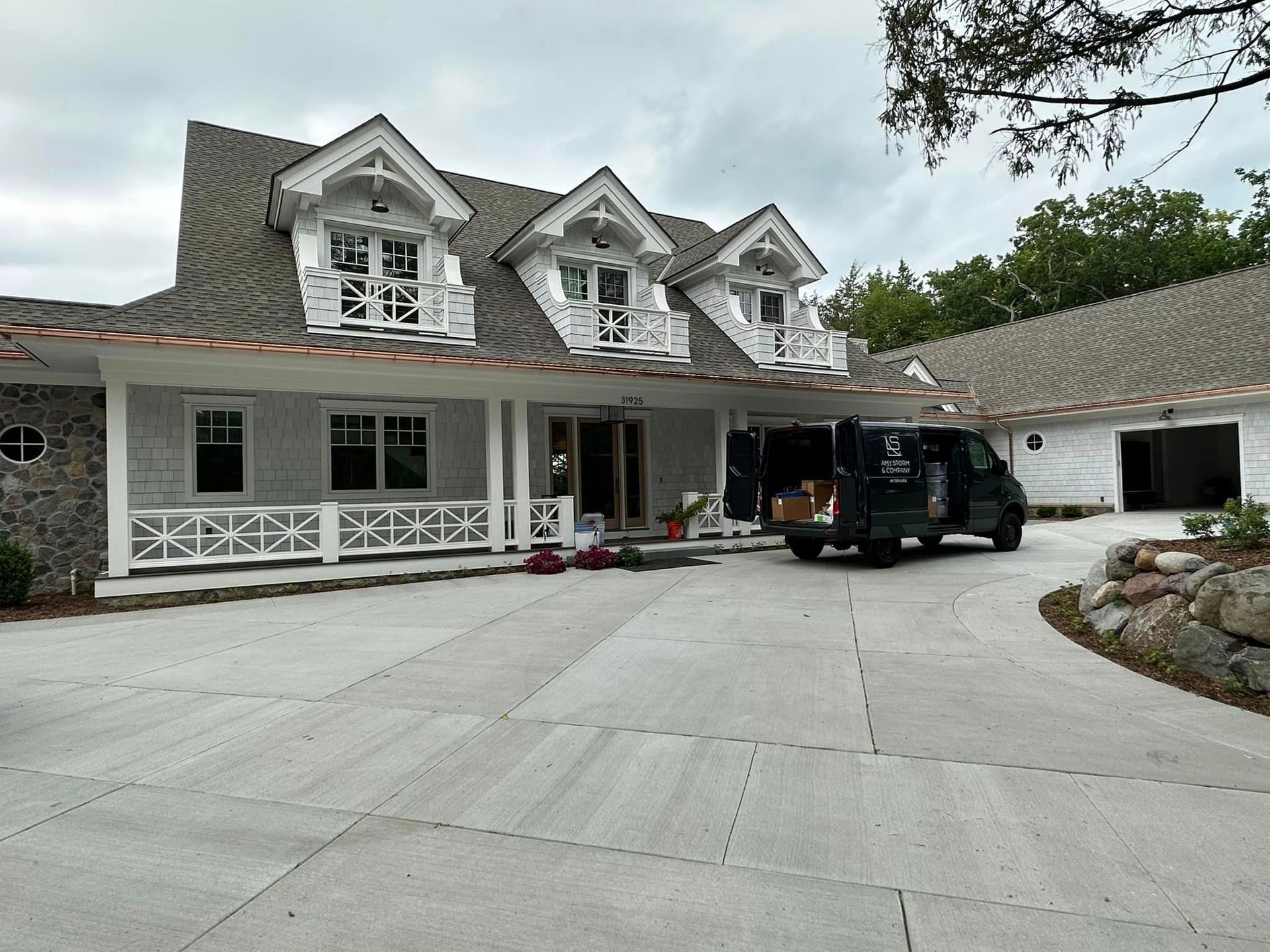 White house with decorative dormers, copper roof, and a black van parked in the driveway.