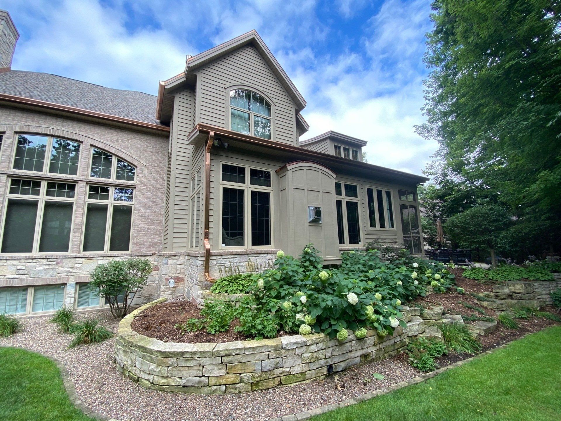Stone home exterior with a garden bed and lawn under a blue sky.