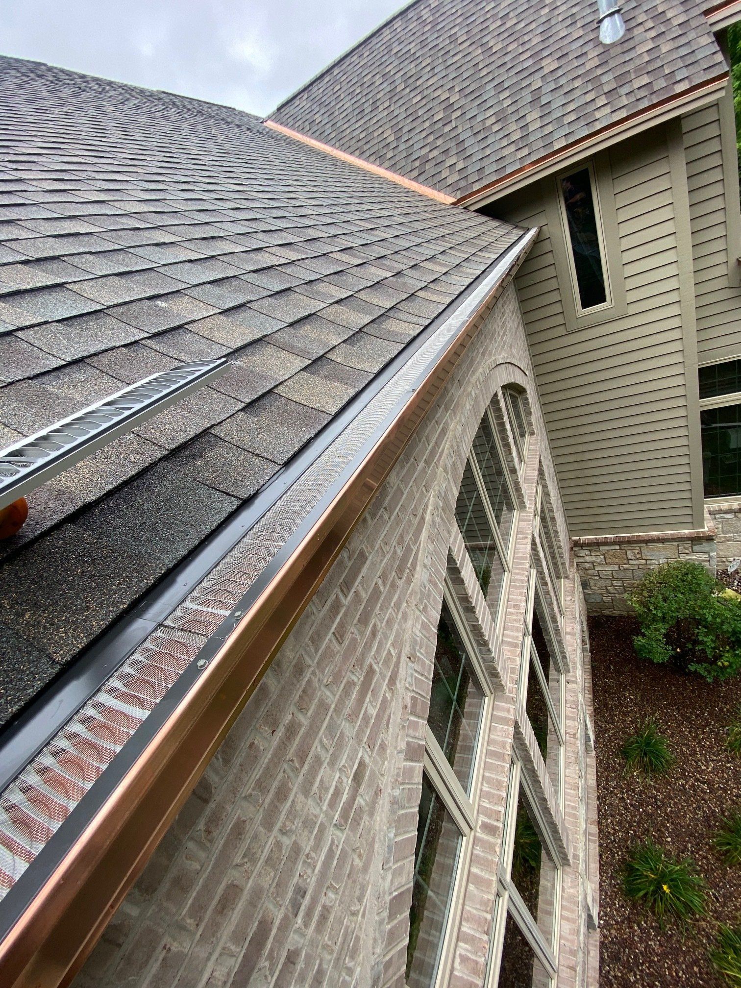 Copper gutters on a home with shingled roof, brick, and windows.