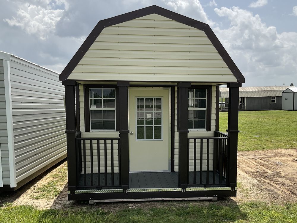 Small black-and-white shed with front porch and door, sitting on grass in an open lot.