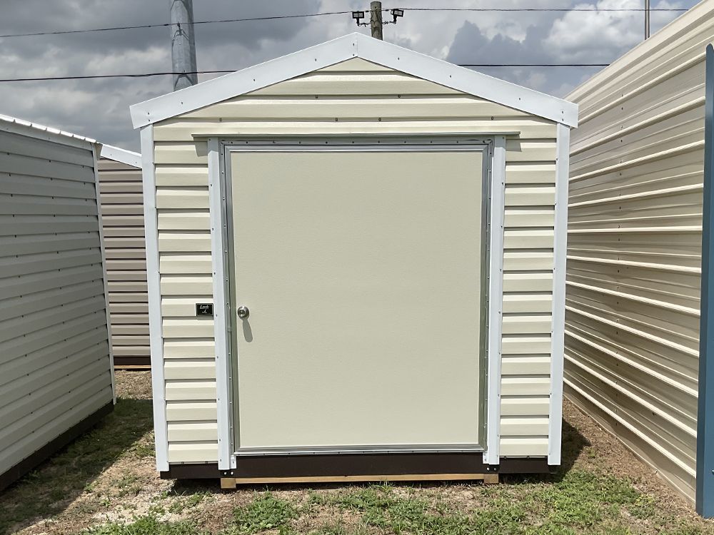 Small white storage shed with a closed beige door between two larger metal buildings.