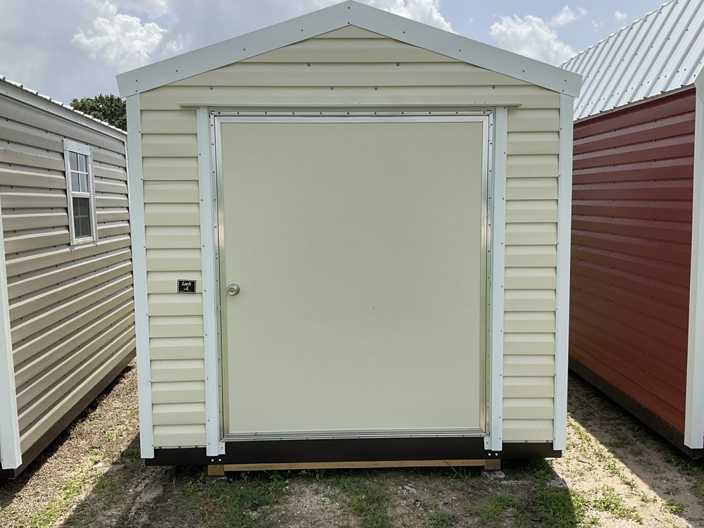 Small white shed with a closed roll-up door, flanked by other storage units outdoors.