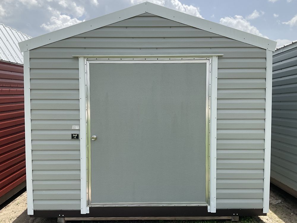 Gray storage shed with white trim and a centered double door on a gravel lot