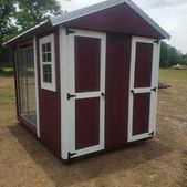 Small maroon garden shed with white trim and windows on a grassy outdoor lot