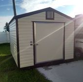 Small white and brown outdoor shed with a gabled roof and double doors on a grassy yard.