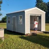 Person standing in the doorway of a small white shed in a grassy yard