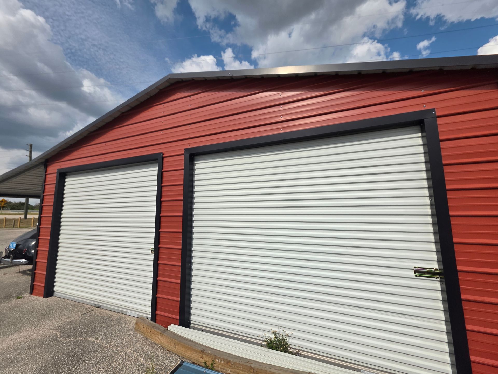 Red garage building with two white roll-up doors under a cloudy sky