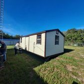 Small cream-and-green portable building on a grassy lot under a bright blue sky