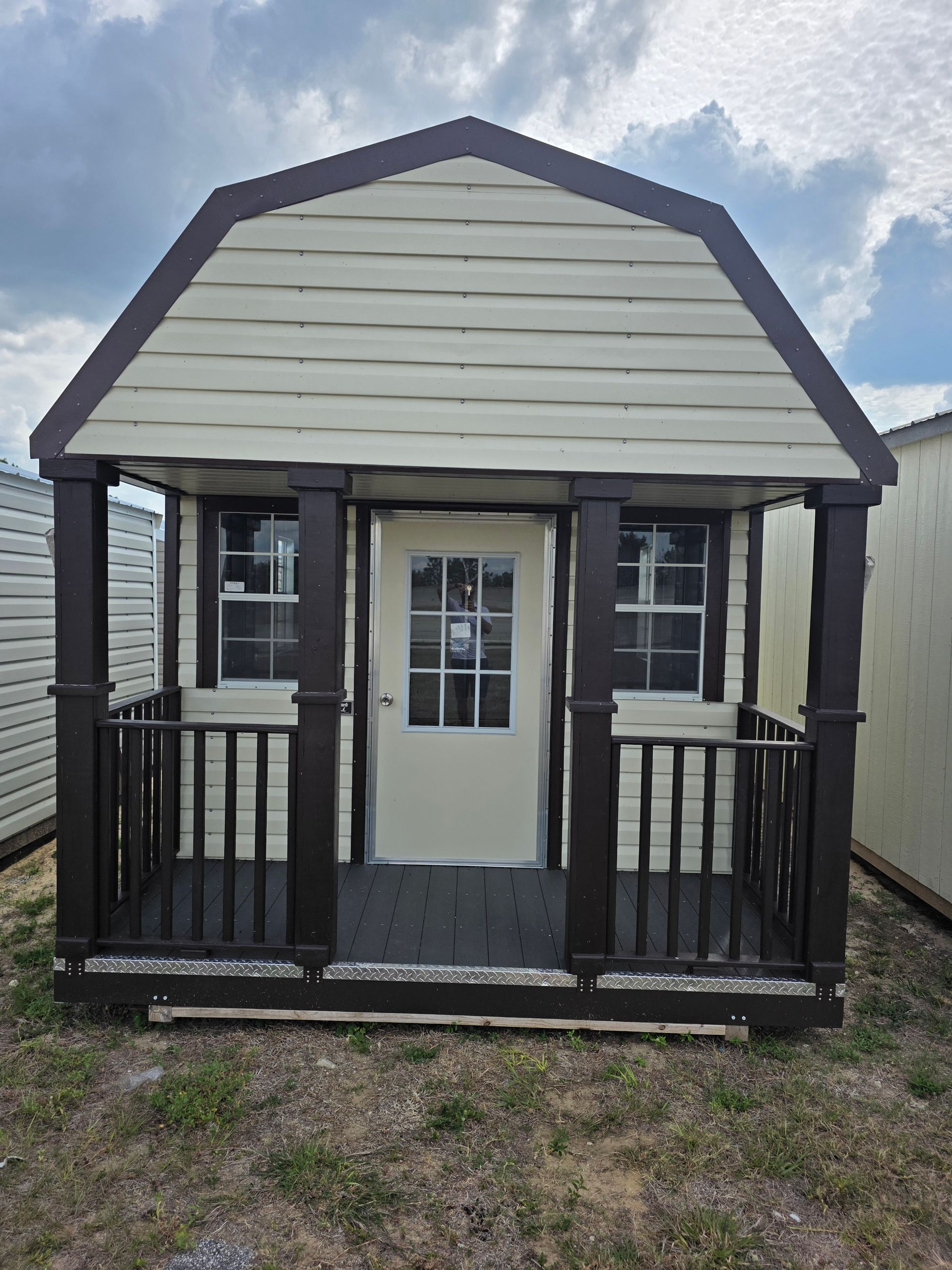 Small beige and black porch shed with a white door and windows on a gravel lot