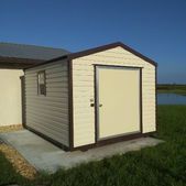Small beige and brown shed-like building on a concrete slab under a clear blue sky