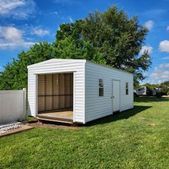 White backyard storage shed with open doors on a grassy lawn under a blue sky