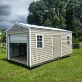 Beige shed with white trim and open garage-style front on a grassy lawn under trees