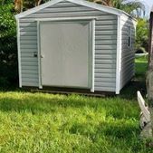 White garden shed with double doors on a grassy lawn, surrounded by greenery.