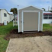 Small beige backyard shed with white trim beside a concrete patio and grass.