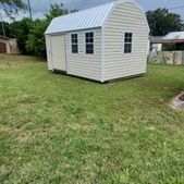 Small beige shed with white trim and a gray roof sitting on a grassy backyard lawn