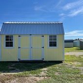 Yellow shed with white trim and double doors on a grassy lot under a blue sky