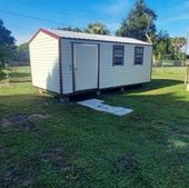 Small beige portable shed with white roof and dark trim sitting on a grassy lawn.