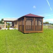 Gazebo with red roof and screened sides on a grassy lawn under a blue sky
