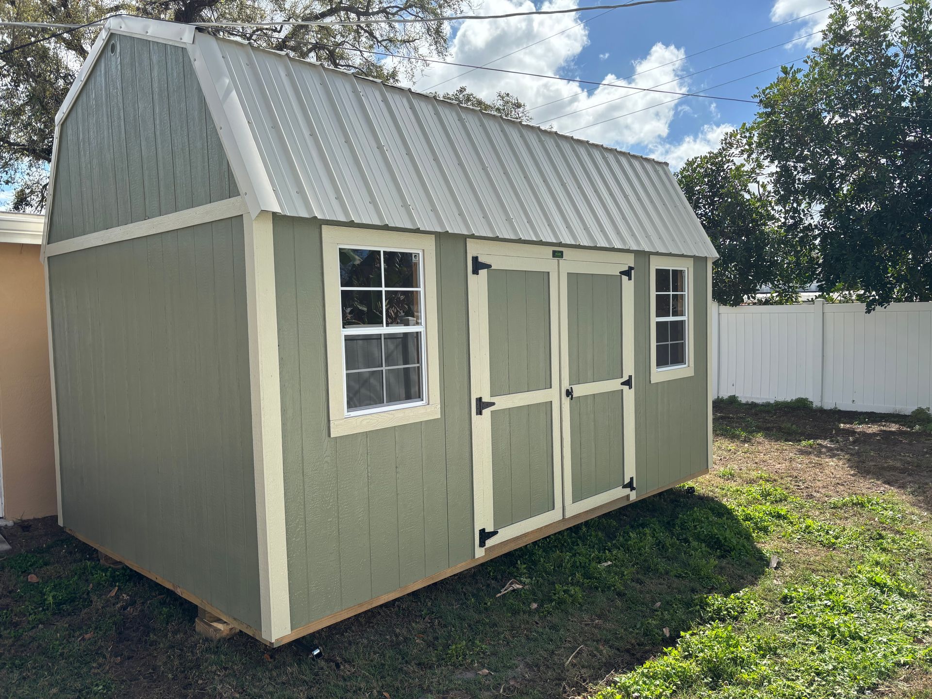 Small beige and green garden shed with white trim and double doors on a grassy yard