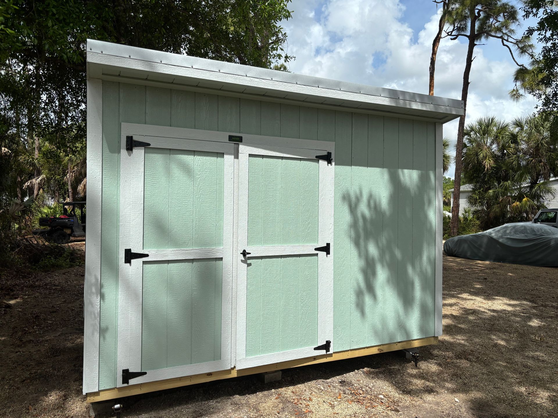 Light green outdoor storage shed with double white doors and black hinges on a wooden base.