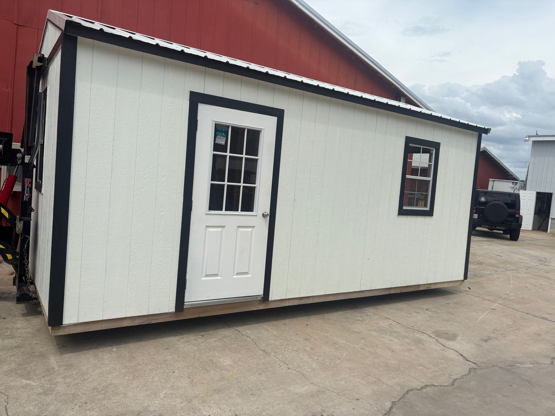 Small white building with red roof, black trim, and a white door on a paved lot.