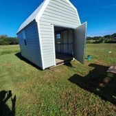 Small white shed with open front doors on a grassy field under a blue sky.