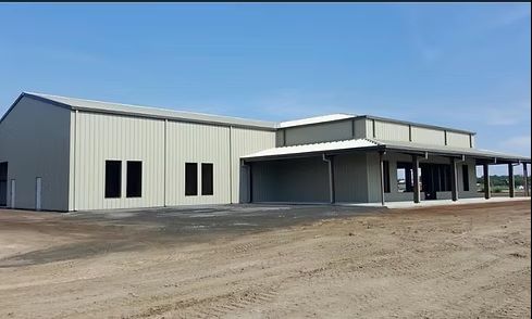 Large metal warehouse building with a covered loading dock on a dirt lot under a clear blue sky