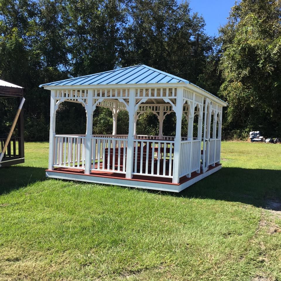 White gazebo with blue roof on a grassy lawn, surrounded by trees in a sunny yard