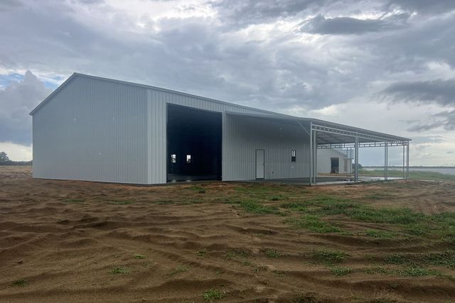 Large white metal barn on a muddy rural lot under a cloudy sky