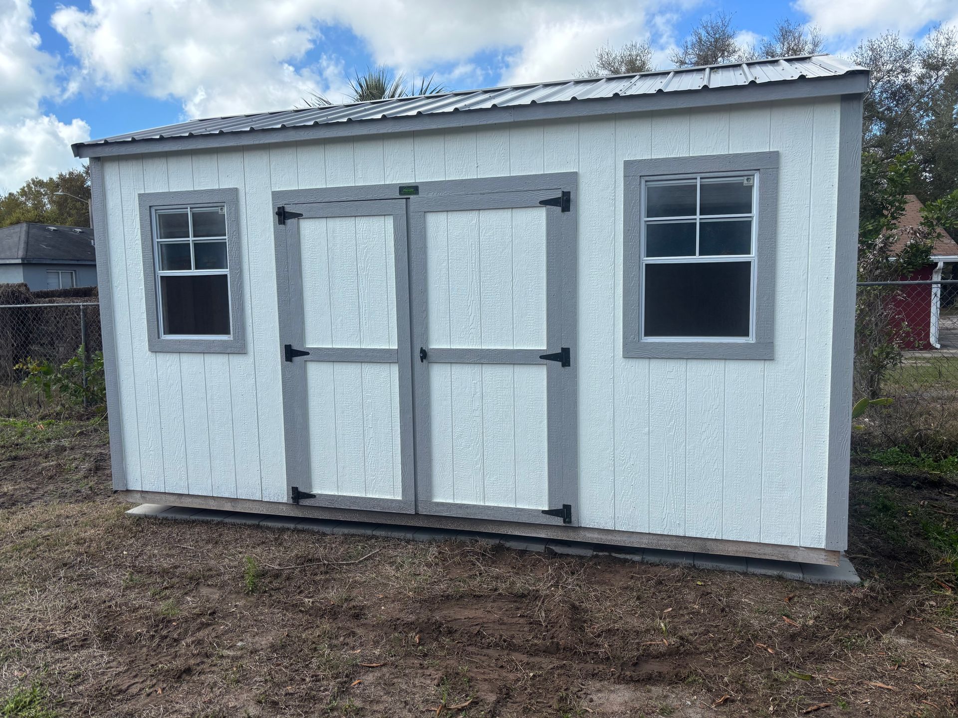 White backyard shed with double doors and two windows under a cloudy sky