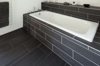 A bathtub is surrounded by black tiles in a bathroom.