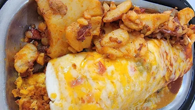 A close up of a burrito with potatoes and cheese on a plate.