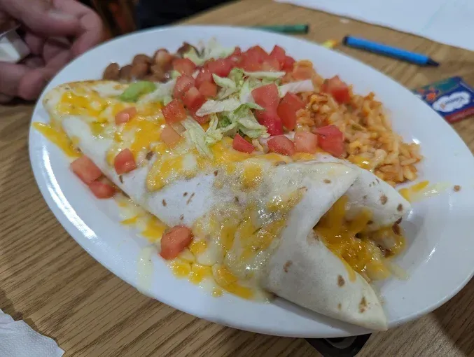 A burrito with cheese , tomatoes , lettuce and rice on a white plate.