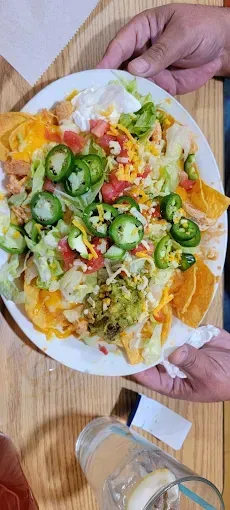 A person is holding a plate of nachos on a table.