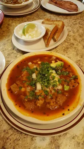 A bowl of soup with a side of toast and sour cream on a table.