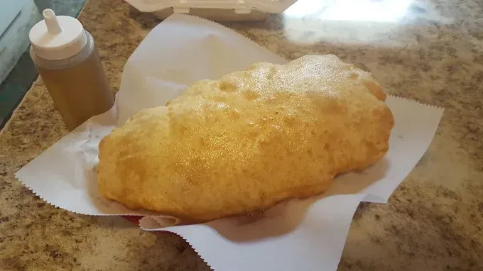 A fried food item is sitting on a paper towel on a table next to a bottle of sauce.