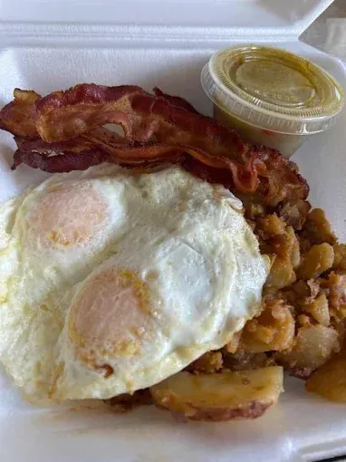 A styrofoam container filled with eggs , bacon and potatoes.