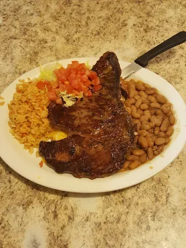 A white plate topped with a steak , beans , rice and tomatoes.
