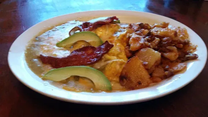 A plate of food with avocado , bacon and potatoes on a table.