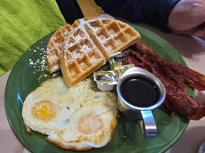 A green plate topped with waffles eggs and bacon