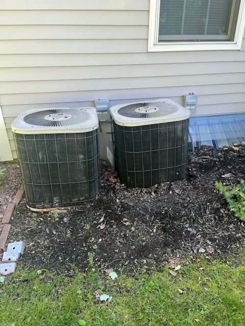 Two air conditioners are sitting next to each other on the side of a house.