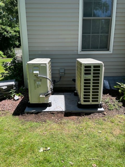 Two air conditioners are sitting next to each other on the side of a house.
