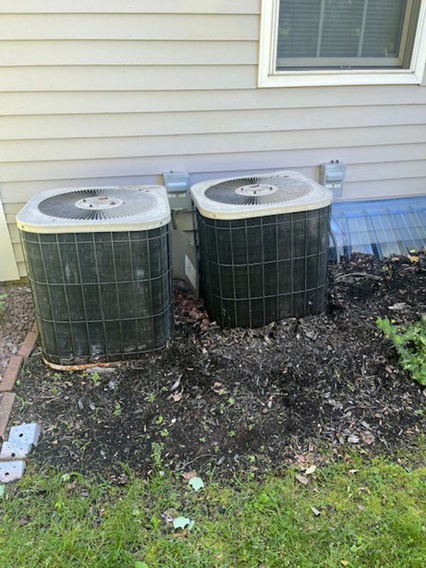 Two air conditioners are sitting next to each other on the side of a house.