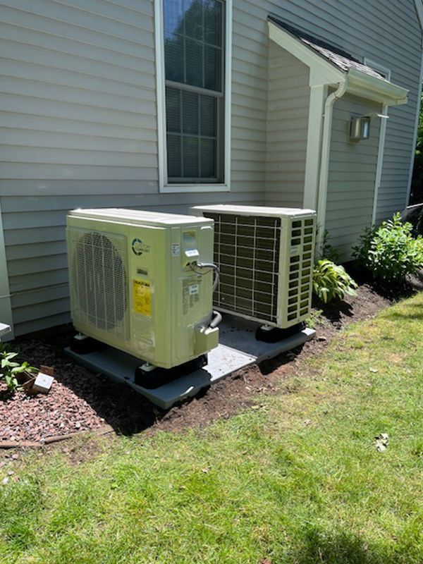 Two air conditioners are sitting on the side of a house.