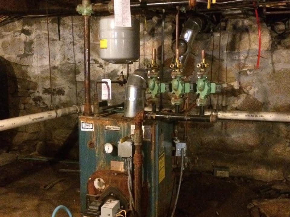 A boiler is sitting in a basement next to a brick wall.